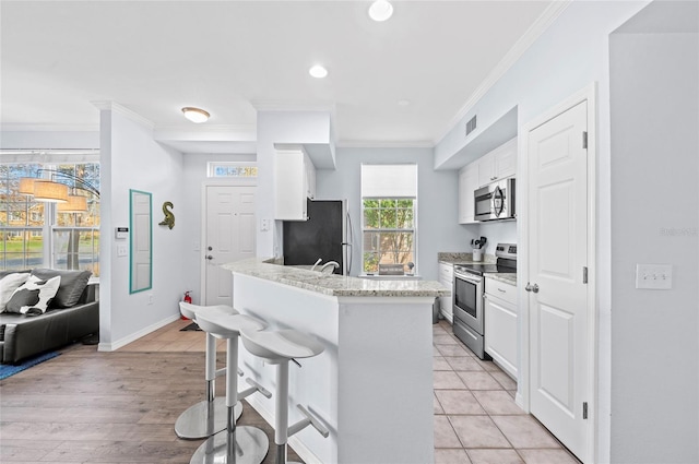 kitchen featuring a breakfast bar, crown molding, light stone countertops, white cabinetry, and stainless steel appliances