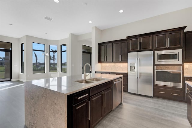 kitchen featuring stainless steel appliances, tasteful backsplash, a center island with sink, and light hardwood / wood-style floors