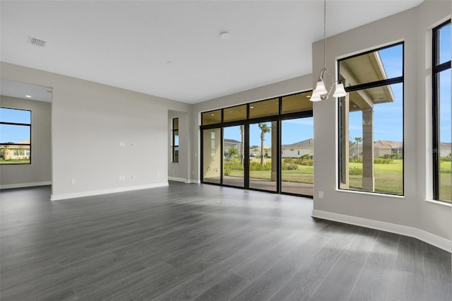 unfurnished living room featuring a notable chandelier, plenty of natural light, and dark wood-type flooring