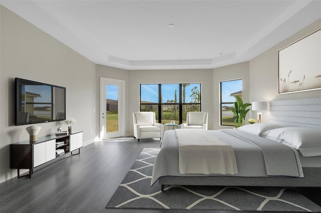 bedroom with dark hardwood / wood-style floors, a raised ceiling, and access to outside