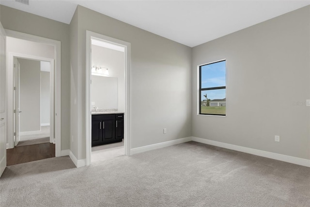 unfurnished bedroom featuring ensuite bathroom and light carpet