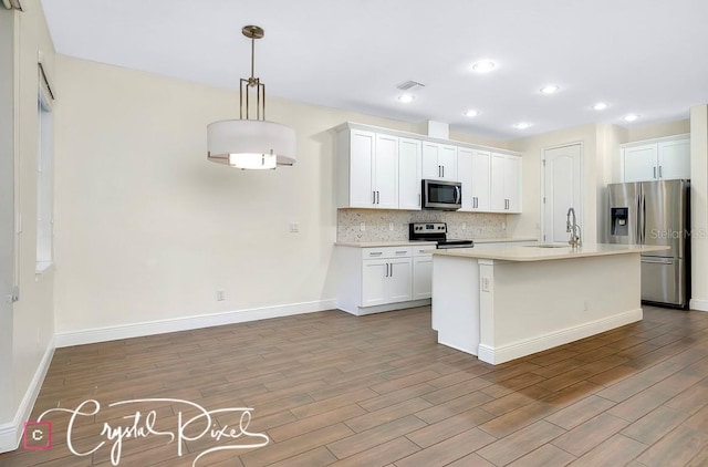 kitchen with white cabinets, light hardwood / wood-style flooring, an island with sink, decorative light fixtures, and stainless steel appliances