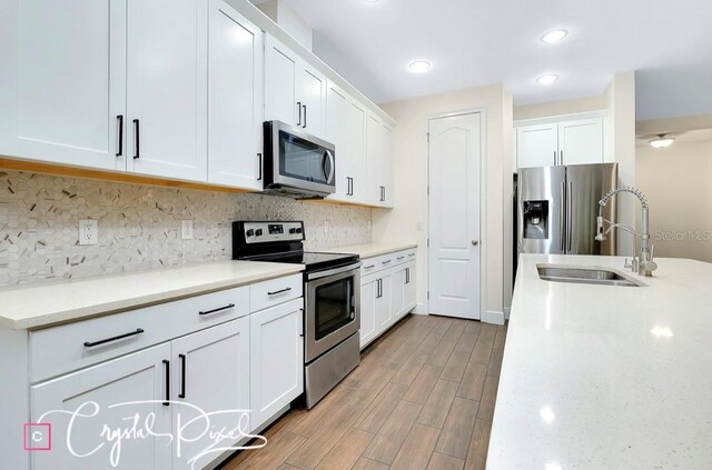 kitchen featuring sink, appliances with stainless steel finishes, light hardwood / wood-style floors, light stone counters, and white cabinetry