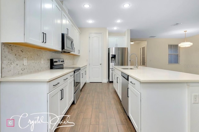 kitchen featuring appliances with stainless steel finishes, wood-type flooring, decorative light fixtures, a center island with sink, and white cabinets