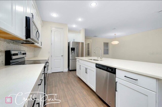 kitchen with pendant lighting, sink, light wood-type flooring, white cabinetry, and stainless steel appliances