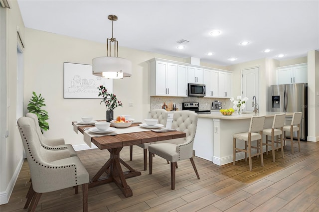 kitchen featuring stainless steel appliances, tasteful backsplash, light hardwood / wood-style floors, decorative light fixtures, and white cabinets