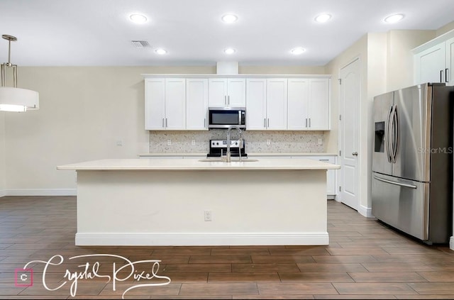 kitchen with appliances with stainless steel finishes, white cabinetry, pendant lighting, and an island with sink