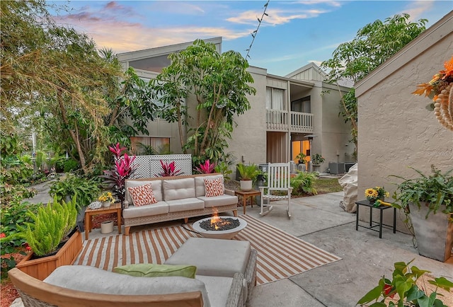 patio terrace at dusk featuring a balcony and an outdoor living space with a fire pit