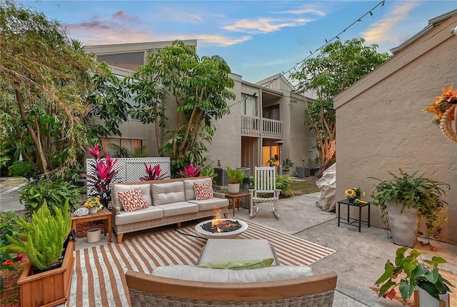 patio terrace at dusk featuring a balcony and an outdoor living space with a fire pit