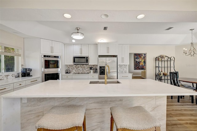 kitchen featuring white cabinetry, sink, hanging light fixtures, stainless steel appliances, and a kitchen breakfast bar