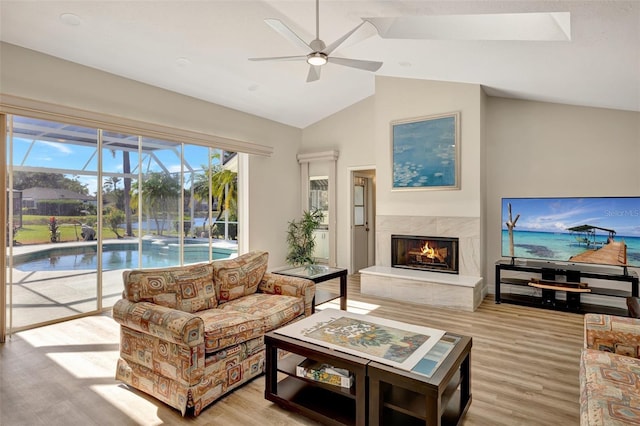 living room featuring ceiling fan, light wood-type flooring, a premium fireplace, and vaulted ceiling