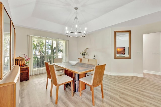 dining space with a raised ceiling, an inviting chandelier, and light wood-type flooring