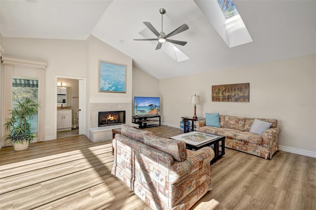 living room featuring ceiling fan, a skylight, high vaulted ceiling, and light hardwood / wood-style flooring