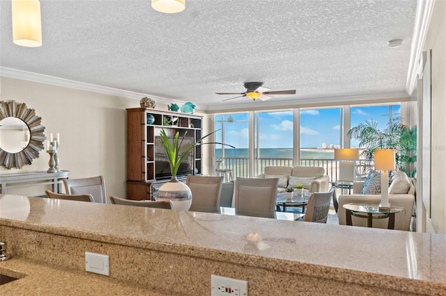 kitchen featuring ceiling fan, a water view, ornamental molding, and a textured ceiling