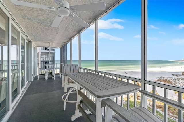 sunroom / solarium featuring plenty of natural light, ceiling fan, a water view, and a beach view