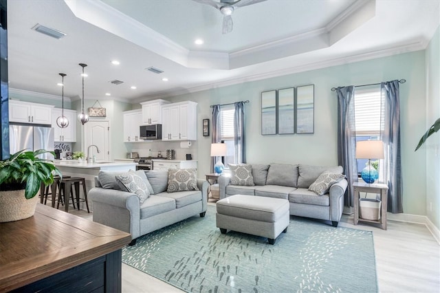 living room with sink, ceiling fan, ornamental molding, and a tray ceiling