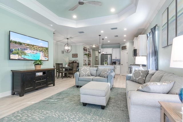 living area featuring a tray ceiling, recessed lighting, light wood-style flooring, ornamental molding, and ceiling fan with notable chandelier