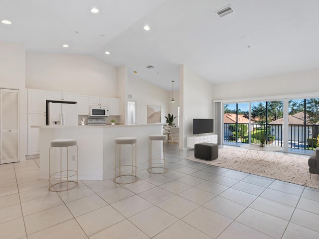 kitchen featuring a kitchen bar, light tile patterned floors, white cabinets, and white appliances