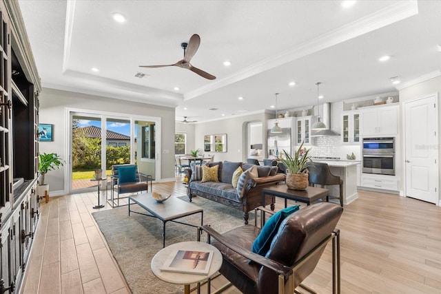 living room with light wood-type flooring, a raised ceiling, and ceiling fan