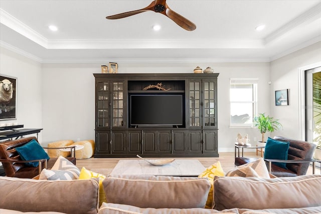 living room with ceiling fan, a raised ceiling, ornamental molding, and light hardwood / wood-style flooring