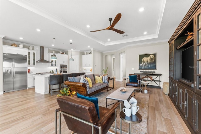 living room with a tray ceiling, ceiling fan, light hardwood / wood-style floors, and ornamental molding