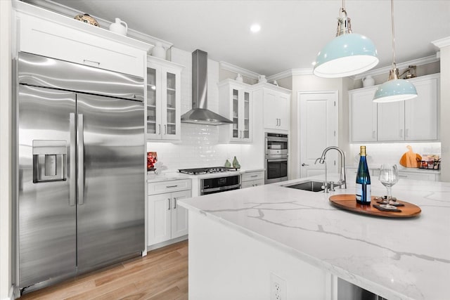 kitchen featuring sink, wall chimney range hood, decorative light fixtures, white cabinets, and appliances with stainless steel finishes