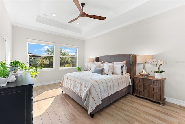 bedroom featuring ceiling fan, a raised ceiling, crown molding, and light hardwood / wood-style flooring