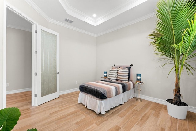 bedroom featuring a tray ceiling, light hardwood / wood-style flooring, and ornamental molding