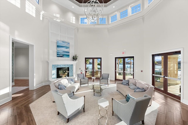 living room with french doors, a high ceiling, crown molding, a chandelier, and hardwood / wood-style flooring