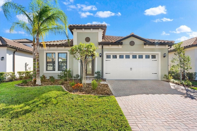 mediterranean / spanish house featuring a tile roof, an attached garage, decorative driveway, a front lawn, and stucco siding