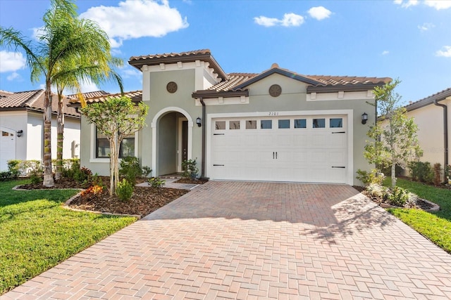 mediterranean / spanish-style home featuring a garage, decorative driveway, a tile roof, and stucco siding