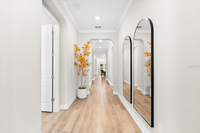 hall with light wood finished floors, visible vents, arched walkways, and crown molding