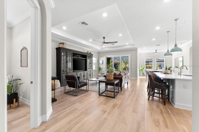 living area with light wood finished floors, a raised ceiling, ceiling fan, crown molding, and recessed lighting