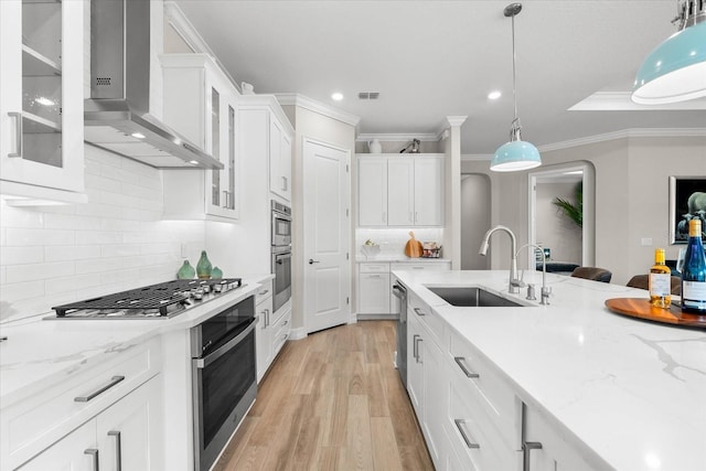 kitchen featuring a sink, white cabinetry, light wood-style floors, wall chimney range hood, and crown molding