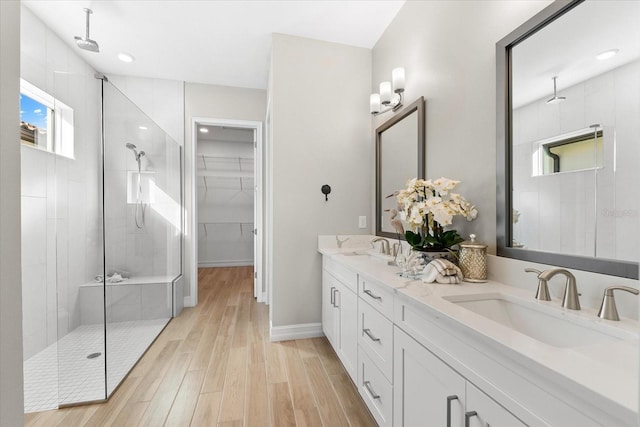 bathroom featuring double vanity, a sink, a shower stall, and wood finished floors