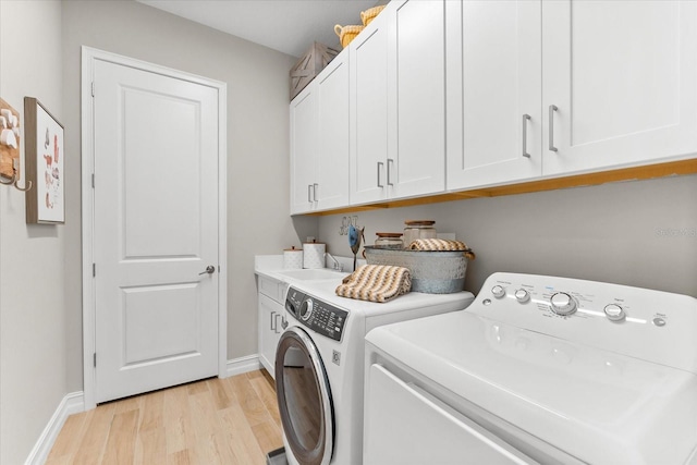 washroom featuring cabinet space, light wood-style flooring, baseboards, and washing machine and clothes dryer