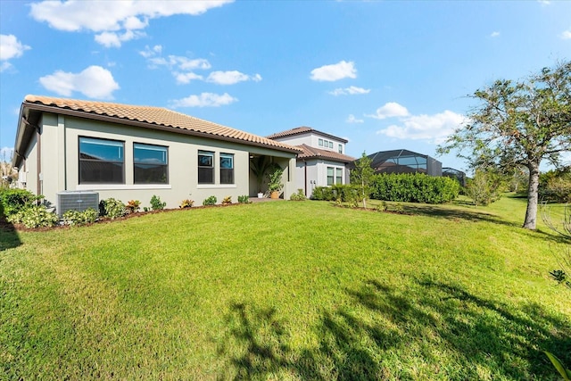 rear view of property with a tile roof, cooling unit, and a yard