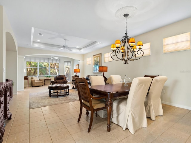 dining space with ceiling fan with notable chandelier, a tray ceiling, and light tile patterned flooring