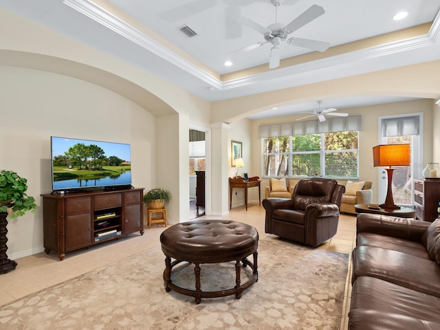 tiled living room featuring decorative columns, a raised ceiling, ceiling fan, and ornamental molding