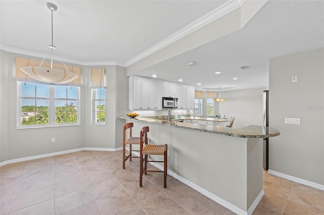 kitchen with decorative light fixtures, white cabinetry, kitchen peninsula, and a wealth of natural light