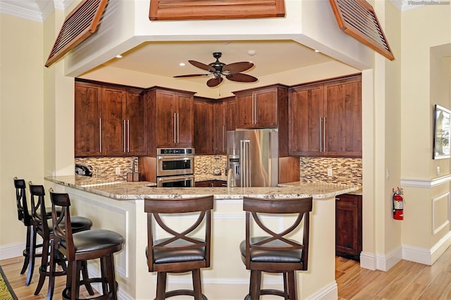 kitchen featuring light stone countertops, kitchen peninsula, decorative backsplash, appliances with stainless steel finishes, and light wood-type flooring