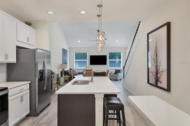 kitchen with a kitchen bar, white cabinetry, sink, hanging light fixtures, and a kitchen island with sink