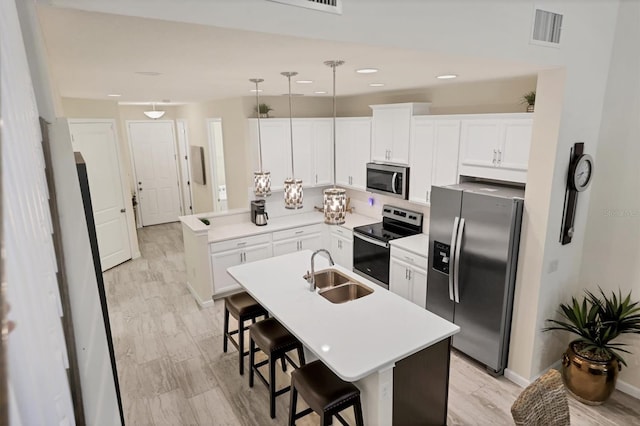 kitchen with pendant lighting, appliances with stainless steel finishes, sink, a kitchen bar, and a kitchen island with sink