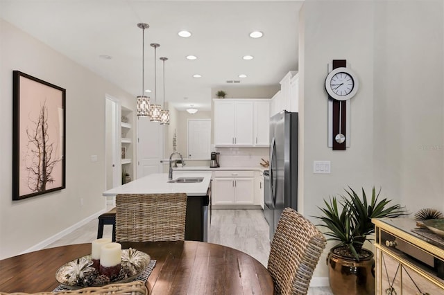 kitchen featuring white cabinets, decorative backsplash, sink, hanging light fixtures, and a kitchen island with sink