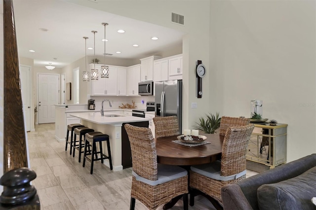 kitchen with white cabinetry, stainless steel appliances, sink, hanging light fixtures, and a center island with sink