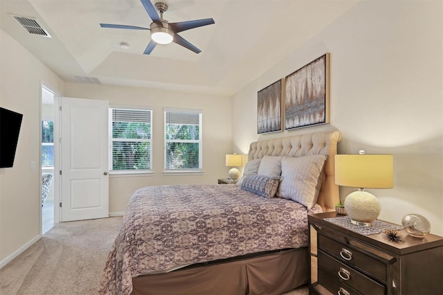 bedroom featuring ceiling fan, light colored carpet, and a tray ceiling