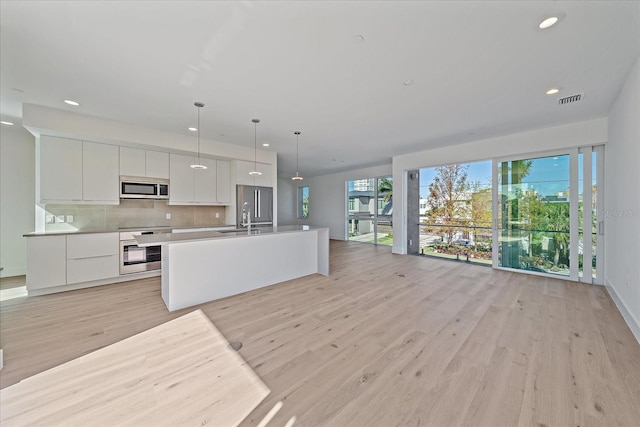 kitchen with white cabinets, sink, hanging light fixtures, light wood-type flooring, and appliances with stainless steel finishes