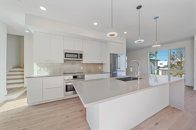 kitchen featuring a kitchen island with sink, sink, light hardwood / wood-style flooring, appliances with stainless steel finishes, and decorative light fixtures