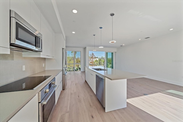 kitchen featuring white cabinets, sink, hanging light fixtures, light wood-type flooring, and appliances with stainless steel finishes