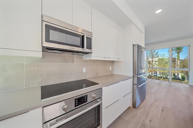 kitchen featuring appliances with stainless steel finishes, backsplash, light hardwood / wood-style flooring, and white cabinetry